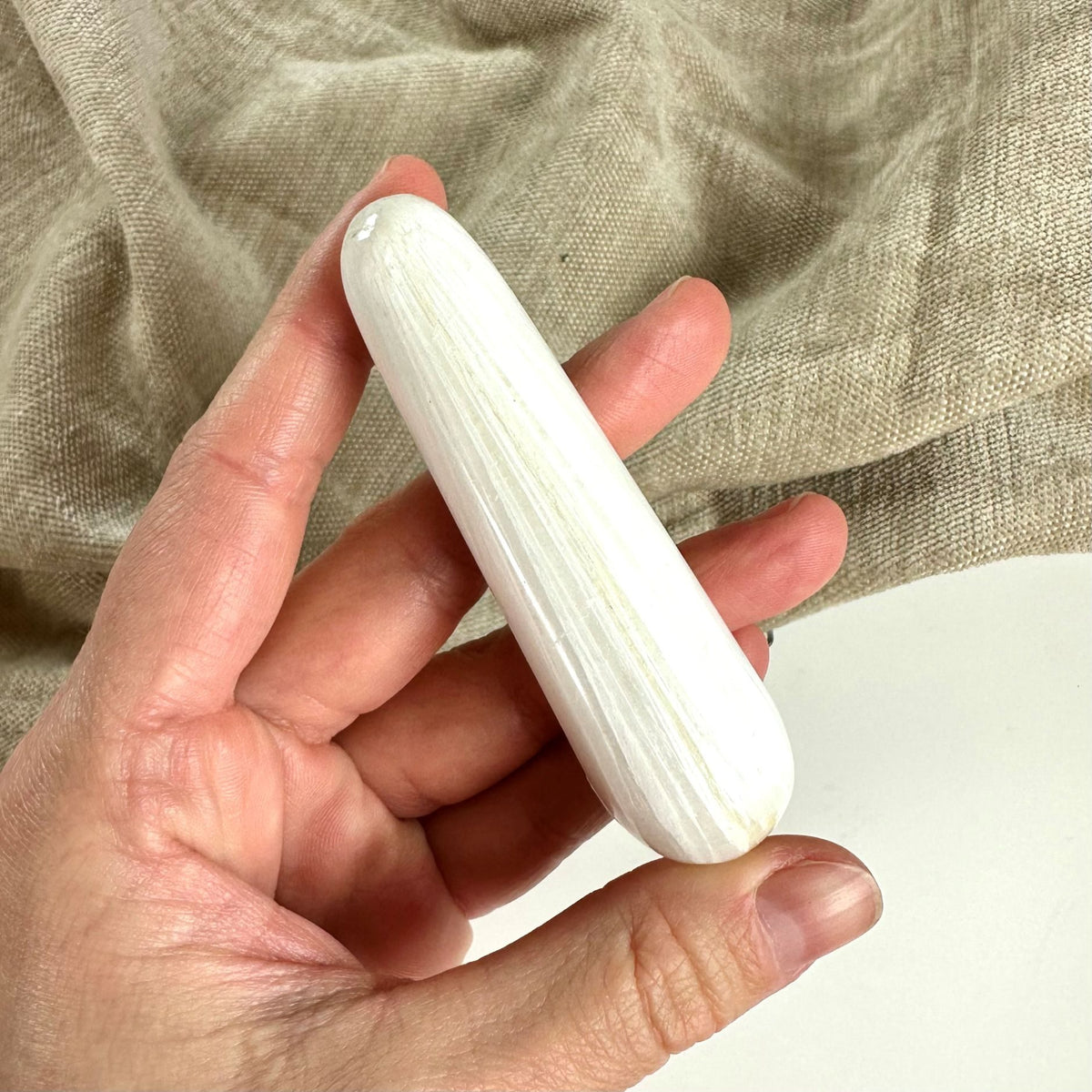 En hånd holder en glat, cylindrisk Scolesit stav mod en baggrund af beige stof.
