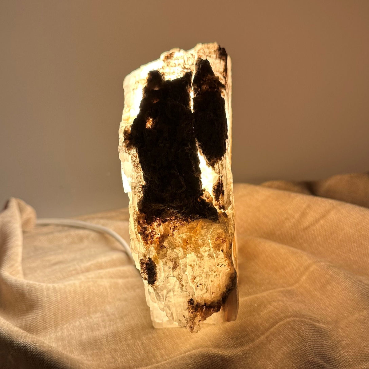 Mexicansk Selenit lampe nr 4 lyser op i en varm glød, stående på et tekstureret stofunderlag.