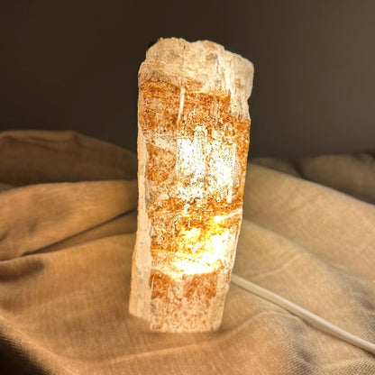 Mexicansk Selenit lampe nr 4 på beige stof, udsender varmt lys i mørkt rum.