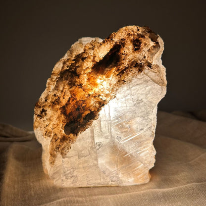Mexicansk Selenit lampe nr 28, der lyser varmt indefra, placeret på et blødt stofunderlag.