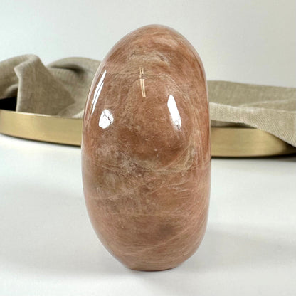 En glat fersken månesten på en lys overflade, baggrund med beige stof og en guldbakke.