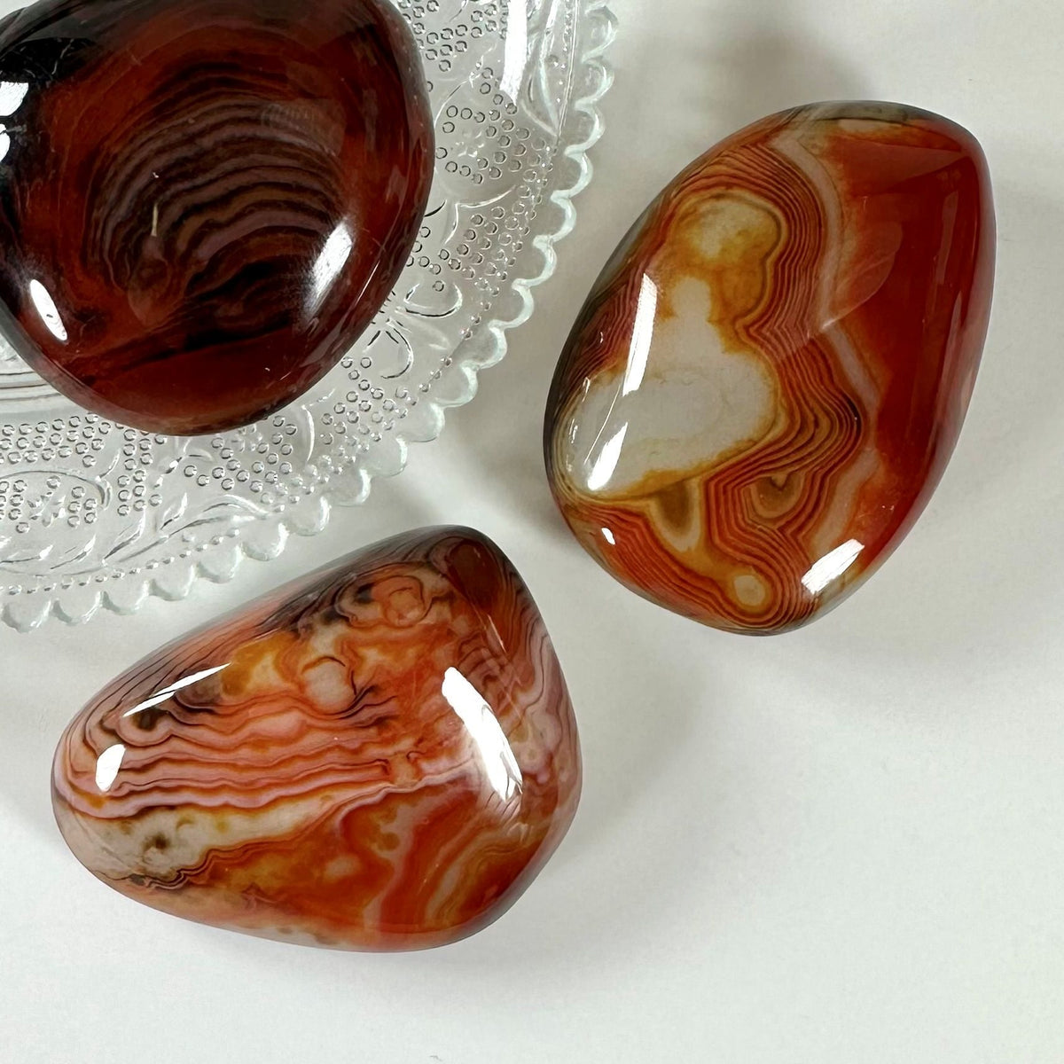 Tre Sardonyx palmsten på en glastallerken, med rige orange og røde toner og naturlige mønstre.