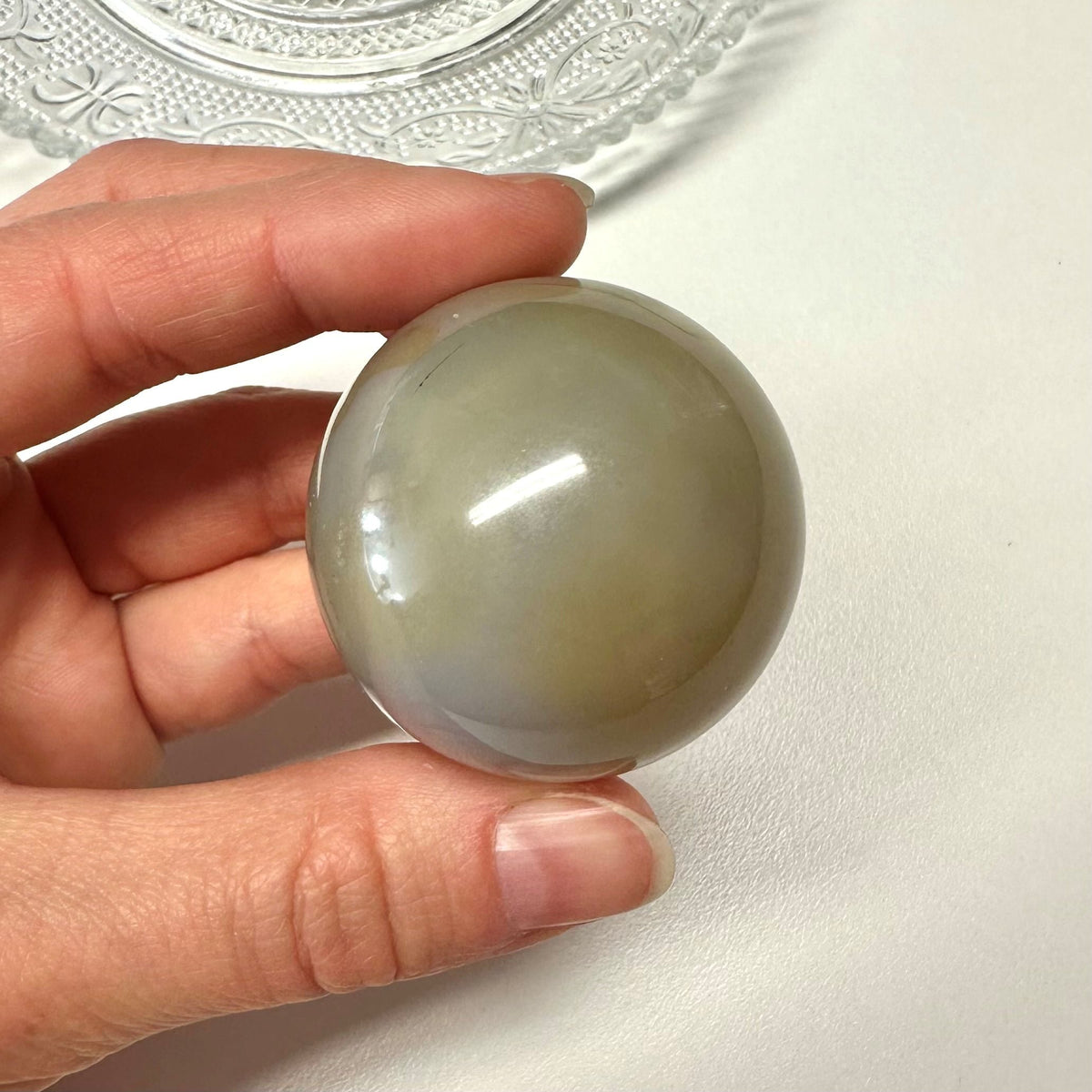 En hånd holder en rund Agat natur kugle mod en lys baggrund med dekorativt glas.