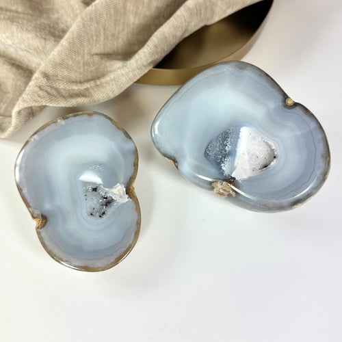 To halve af et agat natur geode sæt med lyseblå og hvide krystalstrukturer på en hvid overflade.