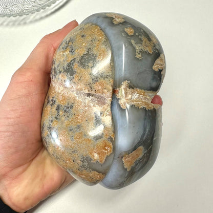 En hånd holder en stor agat natur geode med en grålig overflade og brunlige mønstre.