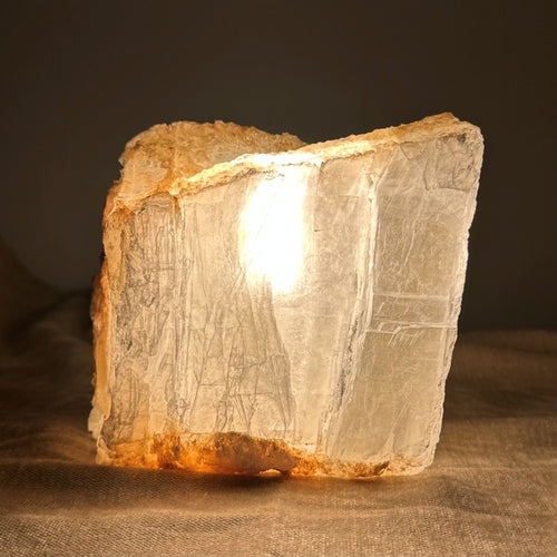 Mexicansk Selenit lampe nr 21. En oplyst, skinnende sten med en varm og gylden glød, der står på en blød overflade.
