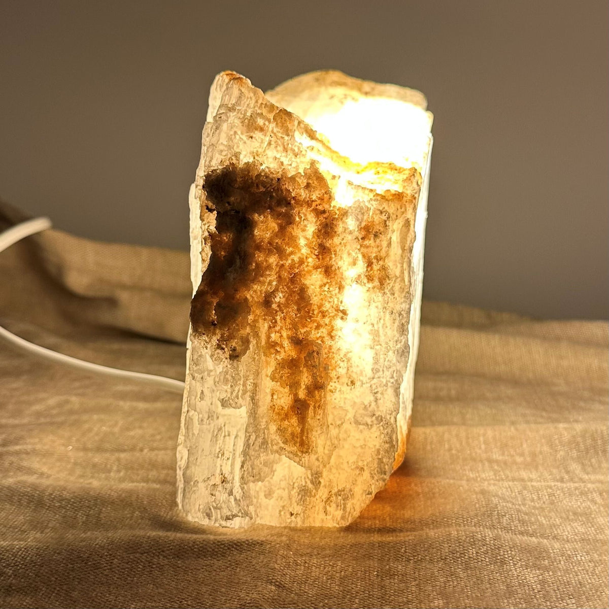 Mexicansk Selenit lampe nr 21 med varmt lys, der oplyser krystallens detaljer på en tekstureret stofbaggrund.