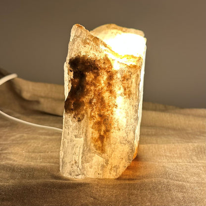 Mexicansk Selenit lampe nr 21 med varmt lys, der oplyser krystallens detaljer på en tekstureret stofbaggrund.