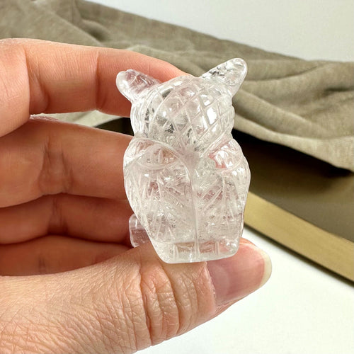 Hånd holder en lille bjergkrystal ugle figur, detaljeret i glitrende mønster.
