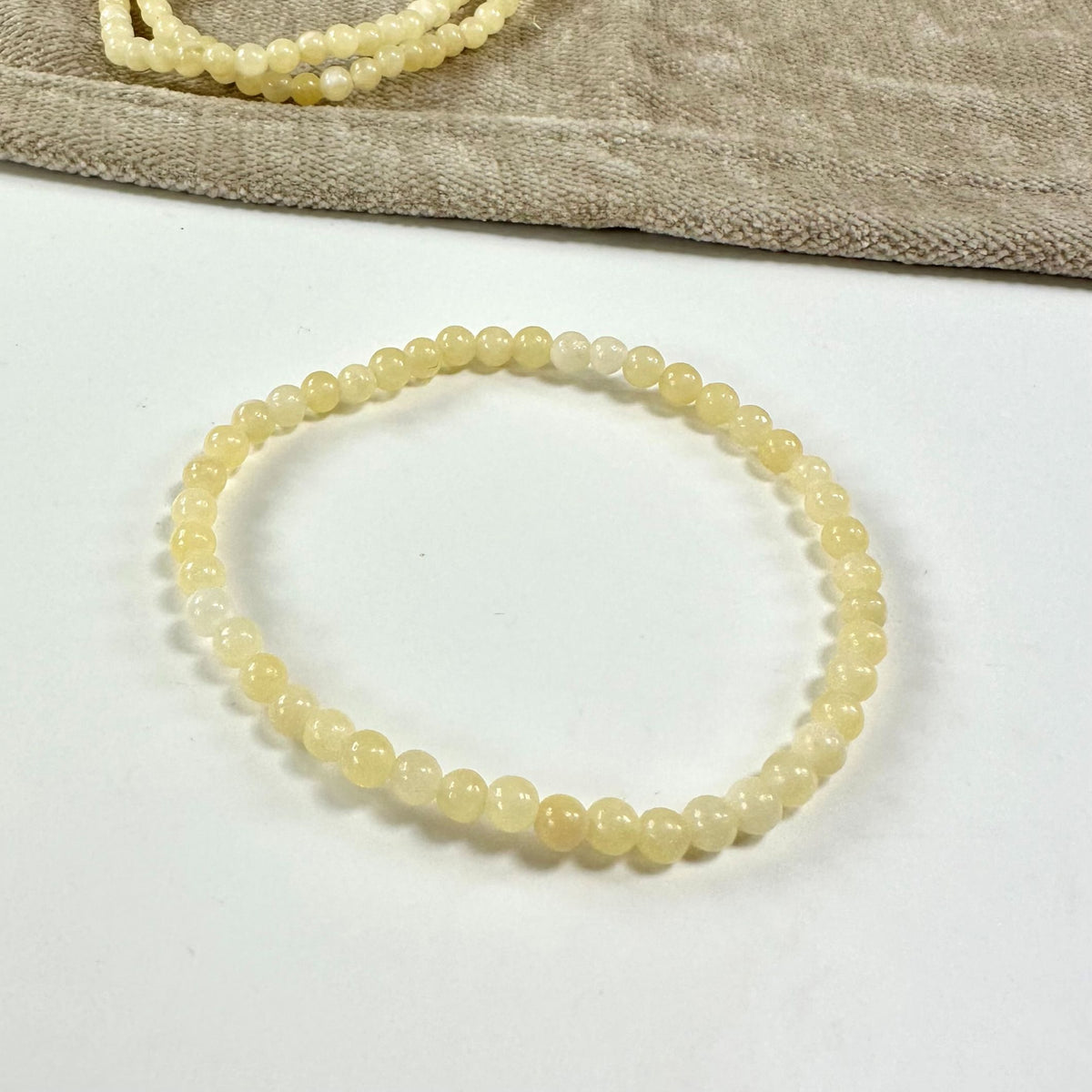 Gul calcit armbånd med perler på en hvid baggrund, delvist dækket af en beige klud.