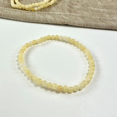 Gul calcit armbånd med perler på en hvid baggrund, delvist dækket af en beige klud.