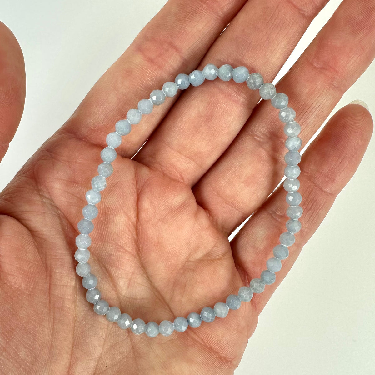 Hånd holder et Angelit armbånd af lyseblå, facetslebne perler.