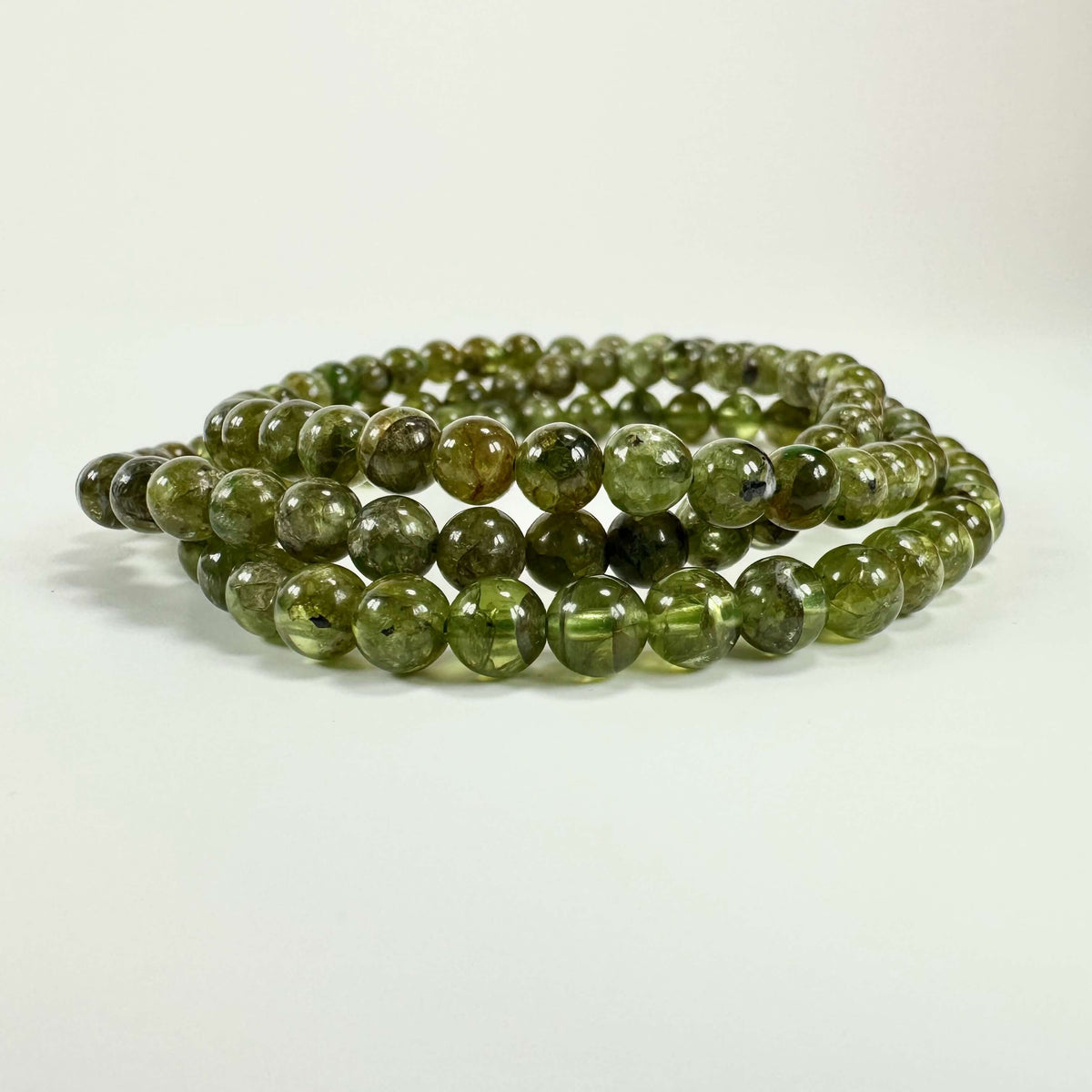 Grønne Peridot armbånd på hvid baggrund, lavet af kugleformede peridotsten i tæt formation.