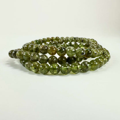 Grønne Peridot armbånd på hvid baggrund, lavet af kugleformede peridotsten i tæt formation.