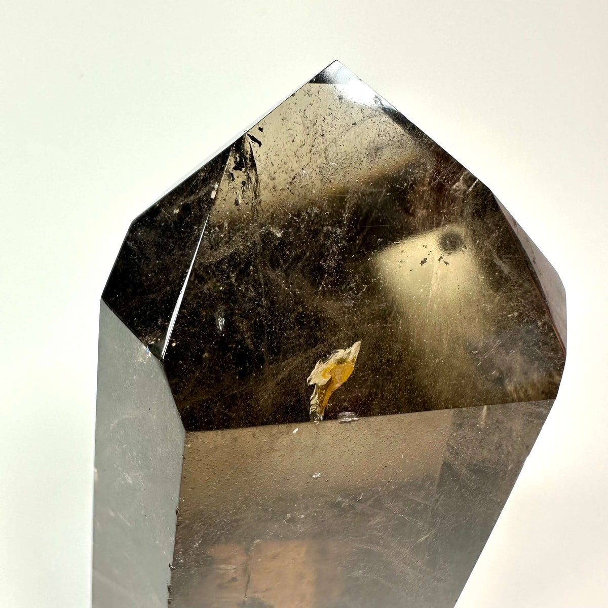 Røgkvarts tårn med glat overflade, der reflekterer lys, ses tæt på mod en hvid baggrund.