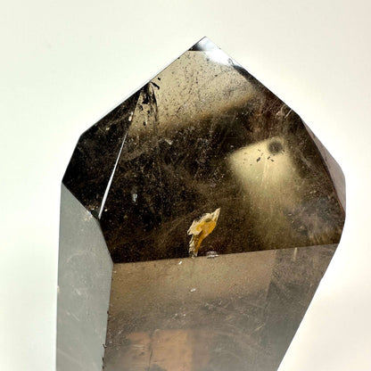 Røgkvarts tårn med glat overflade, der reflekterer lys, ses tæt på mod en hvid baggrund.