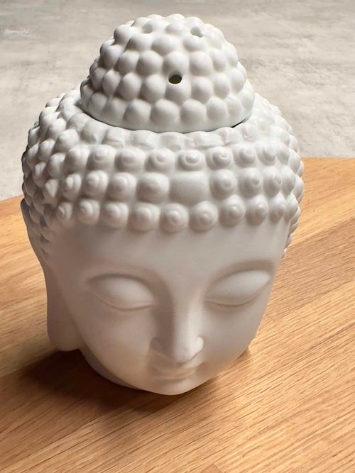 Voksbrænder med Buddha-hoved i hvid keramik på træbord, brugt til aromaterapi.