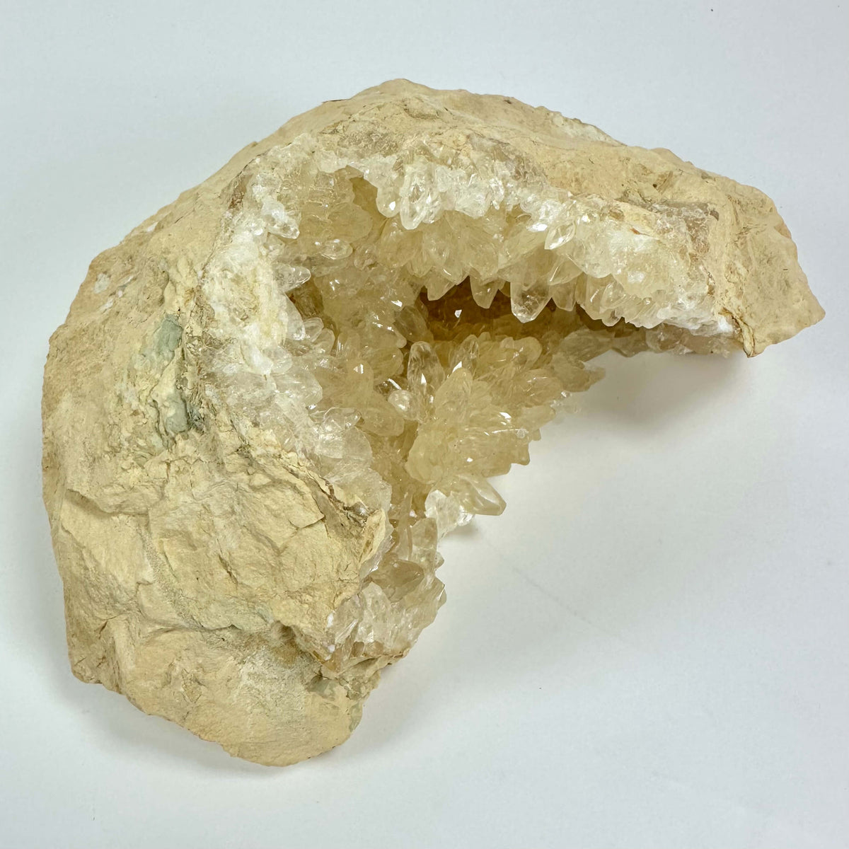 Gul calcit geode med klare krystaller i en åben stenformation mod en hvid baggrund.