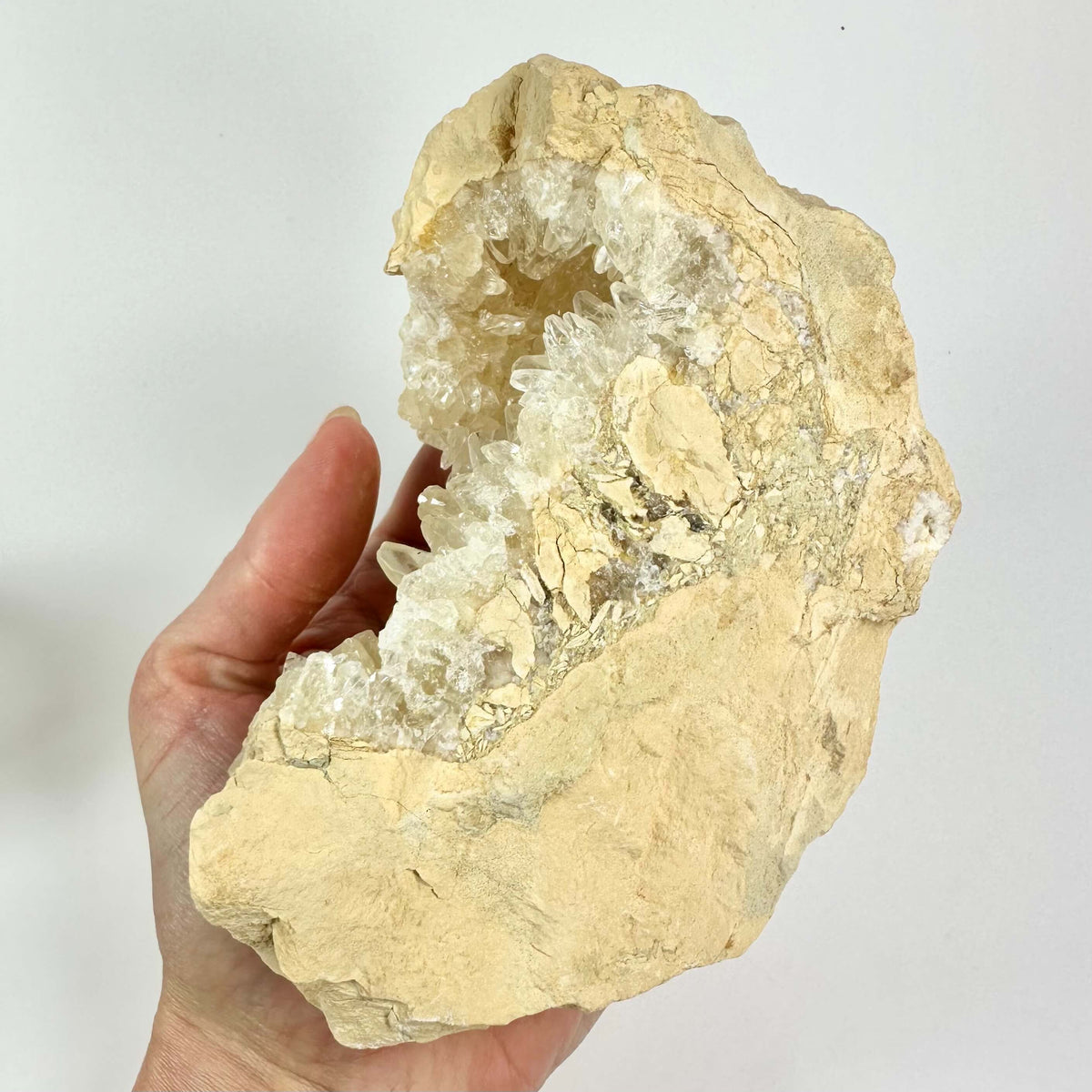 Hånd holder en gul calcit geode, åbnet for at vise krystallerne indeni.