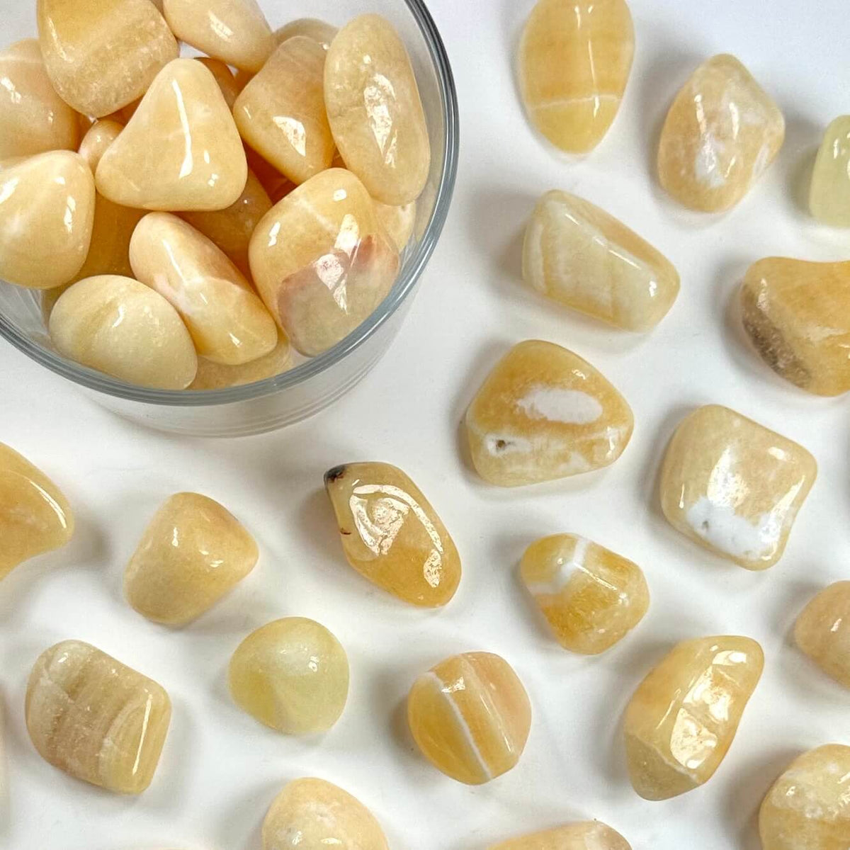 Gul calcit lommesten i glas og spredt på hvid baggrund