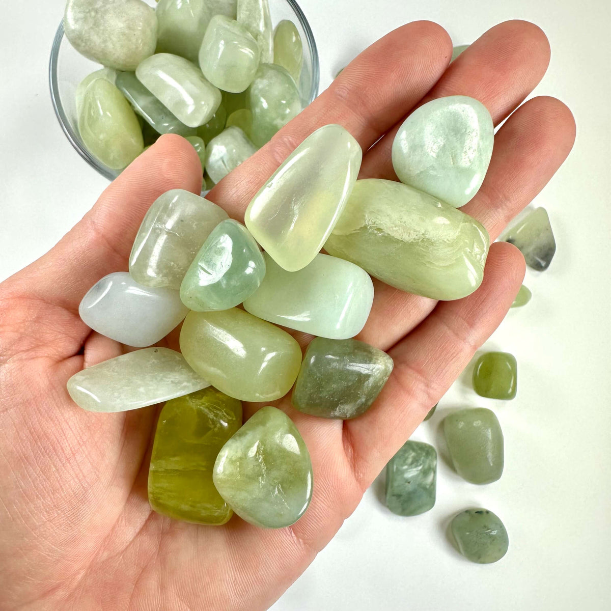 Grøn jade lommesten i en hånd og et glas på en hvid baggrund