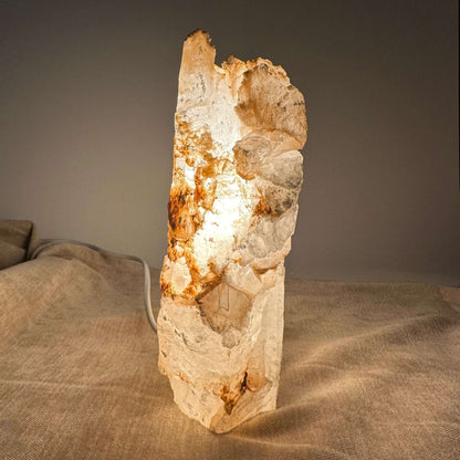 Mexicansk Selenit lampe nr 5 lyser blødt op med sin naturlige stenskønhed på en tekstureret beige overflade.