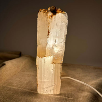 Mexicansk Selenit lampe nr 5 skinner varmt lys på en beige overflade med en ledning ved siden af.