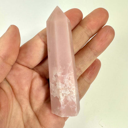 En person holder et Pink opal tårn i hånden mod en lys baggrund.