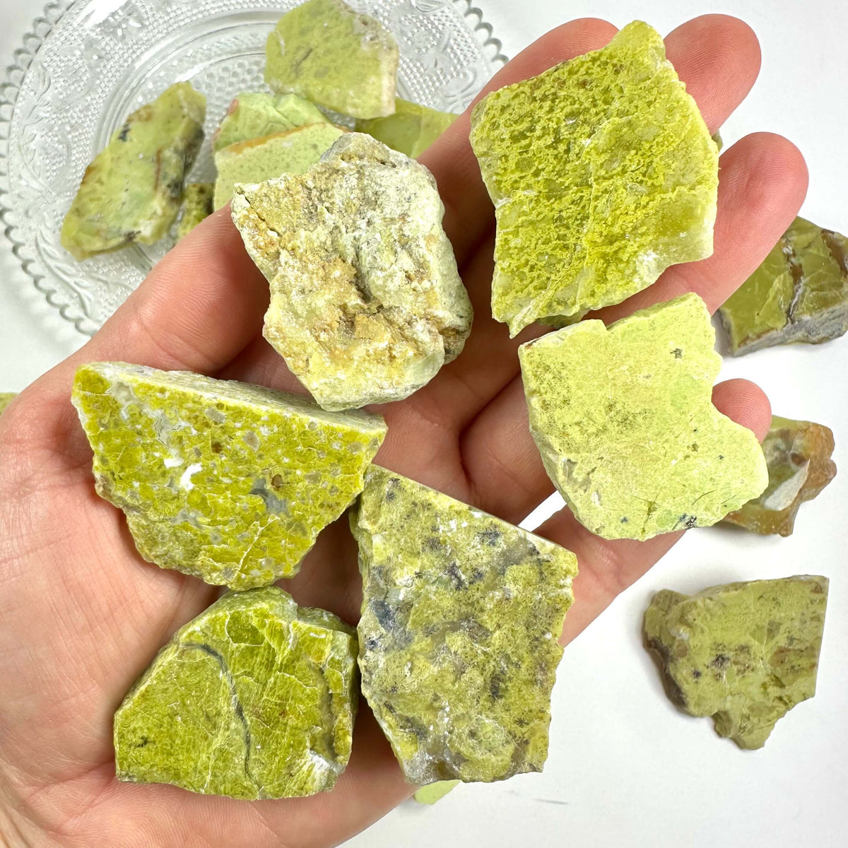 Hånden holder flere grønne mineralsten på en tallerken.