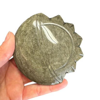 Hånd holder en Guld Obsidian sol og måne skulptur med glat overflade og skulpterede kanter.