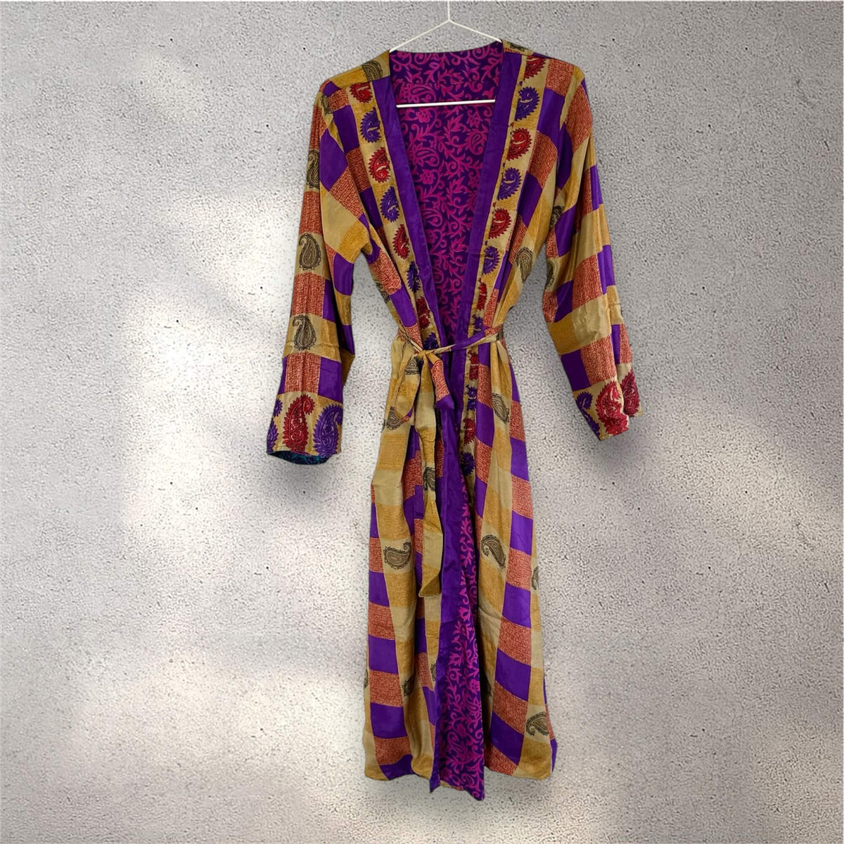 Farverig kimono med lilla, brune og gyldne tern, hænger på en bøjle mod lys væg.