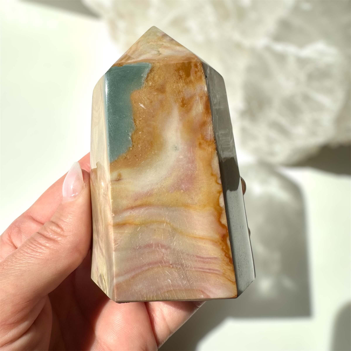 Jaspis polychrome tårn med flerfarvede lag holdt i en hånd mod en utydelig baggrund.