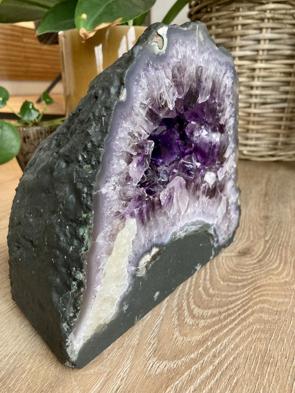 Ametyst grotte på en træbord, omgivet af grønne planter i baggrunden.