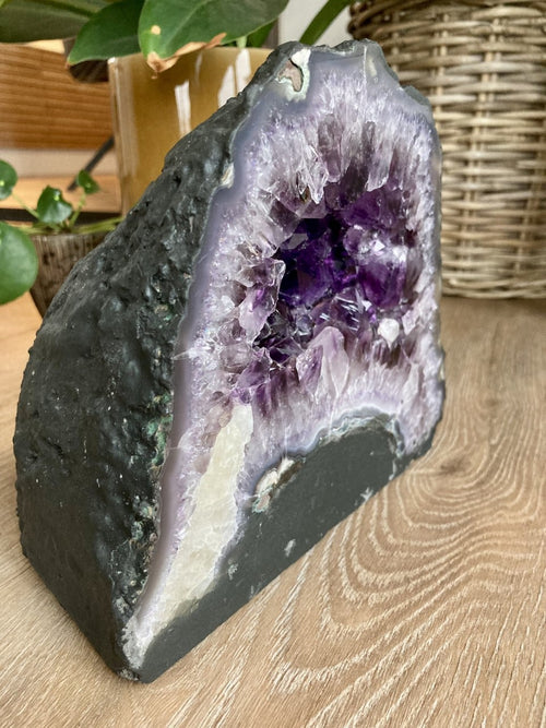 Ametyst grotte på en træbord, omgivet af grønne planter i baggrunden.