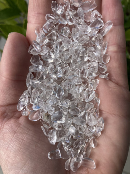 Håndfuld af klare bjergkrystaller mod en grøn baggrund. 100 gram Bjergkrystal mini.