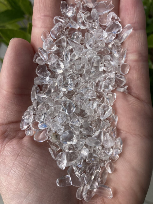 Håndfuld af klare bjergkrystaller mod en grøn baggrund. 100 gram Bjergkrystal mini.