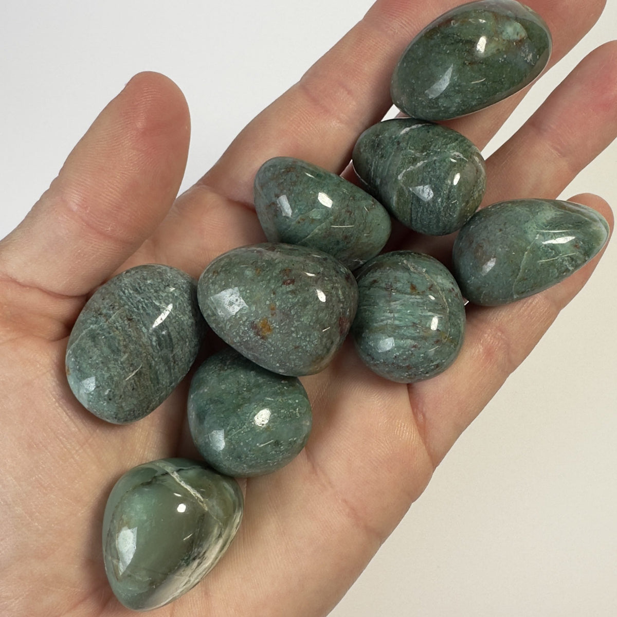 En hånd holder Chrysocolla grønne lommesten.
