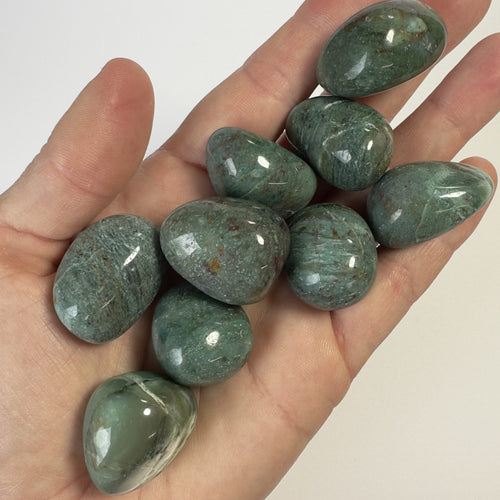 En hånd holder Chrysocolla grønne lommesten.